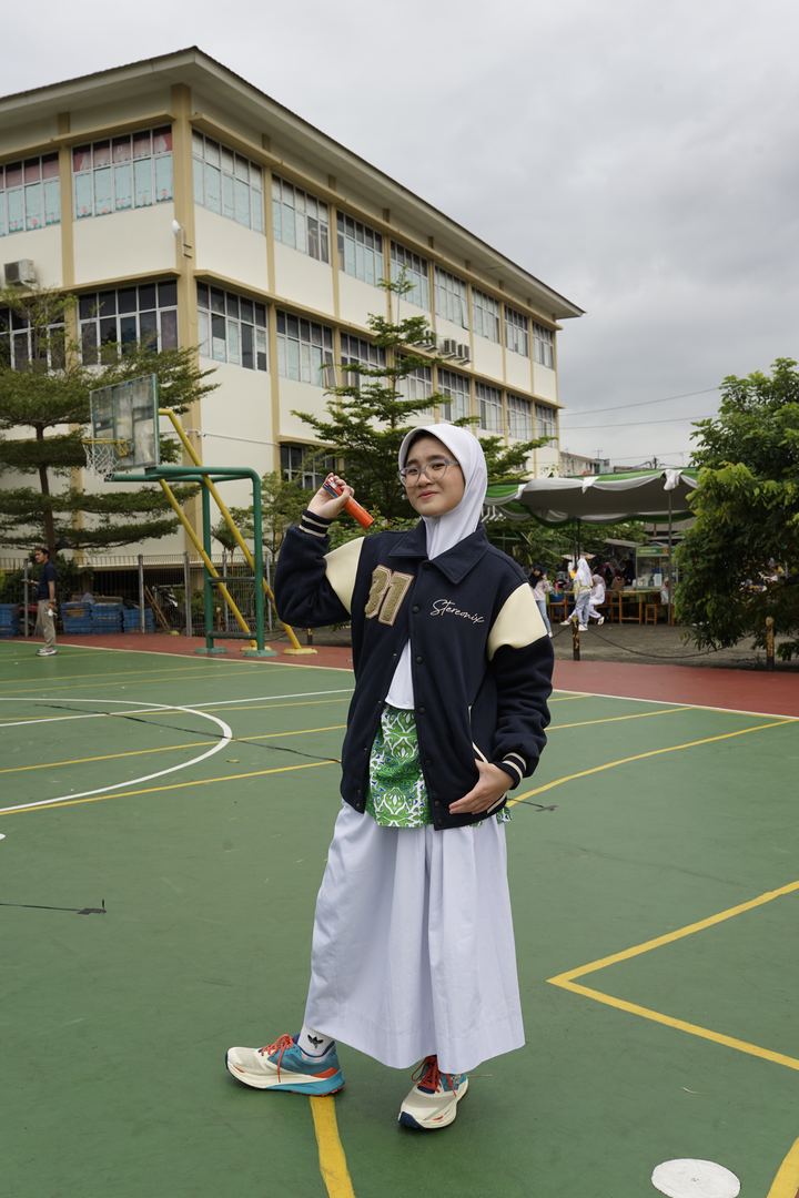 Siswi memakai jaket varsity angkatan di lapangan sekolah